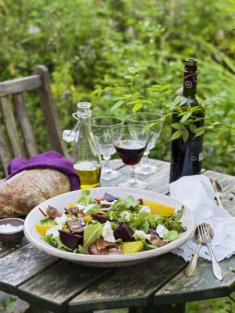Goat cheese salad, bread, olive oil, salt, cutlery and wine on table